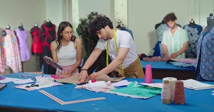 Indian young adult gen z female male man wear tape around neck use tab look screen talk share idea class room place. Tailor girl boy hold pencil do paper pattern create cloth craft dress learn work