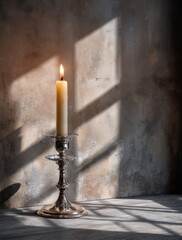 Elegant still life featuring a lit candle in a silver candlestick, bathed in dramatic light and shadow against a textured wall.