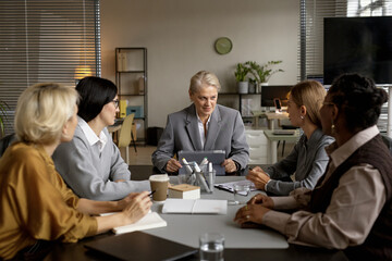 Fototapeta premium Senior Caucasian Woman Leading Diverse Team Meeting in Modern Office Setting