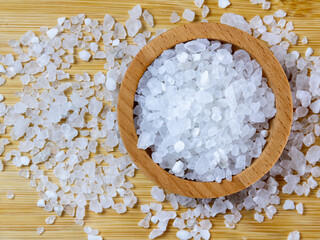 Natural sea salt, scattered in a wooden bowl, on a wooden background.
