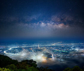 the milky way stretches across the night sky above Chiang mai city, seen from Doi Suthep mountain in northern Thailand, where city lights glow beneath layers of mist in the tranquil landscape.