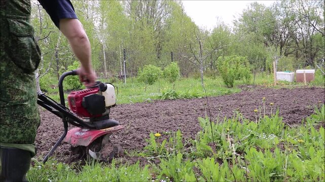 Klin, Moscow, Russia - 05.22.2025: A farmer starts a cultivator, starting the motor to loosen the soil on a farm. Spring agricultural work - horizontal color video, male hands