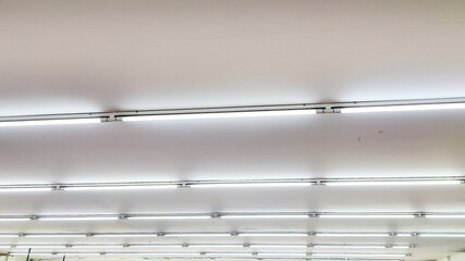 A series of LED tube lights installed on a ceiling. A row of lights are hanging from the ceiling in a room. The lights are white and are evenly spaced.
