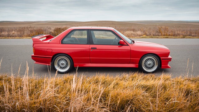 Red 1980s BMW coupe on a rural road on autumn day. Side view of BMW M3 - performance version of german sport coupe. Ukraine - October 19 2024