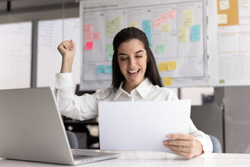 Joyful young businesswoman read business papers raise arm in triumph