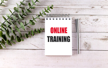 Notebook with online training text on wooden table with pen and plant representing remote education or digital learning