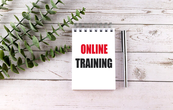 Notebook with online training text on wooden table with pen and plant representing remote education or digital learning
