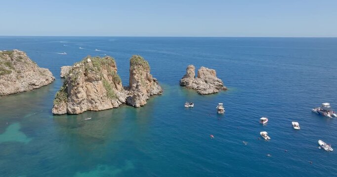 Aerial view of the Faraglioni rocks located in the Bay of Scopello, in the province of Trapani, Sicily, Italy. There are boats on holiday among the cliffs.
