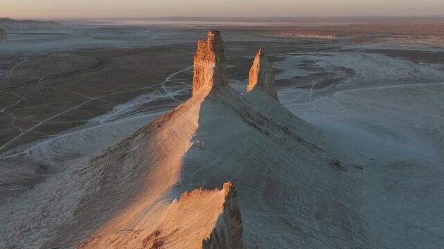 Aerial view of the Bozhira rock formations, where towering cliffs meet the vast desert, creating a stark contrast of light and shadow, Bozhira, Mangystau Region, Kazakhstan.