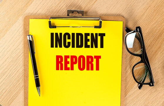 Clipboard with incident report text on yellow paper next to pen and glasses on wooden desk