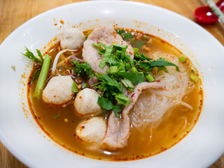 Thai Tom Yum Glass Noodle Soup with Pork Fishballs and Fresh Herbs in White Bowl