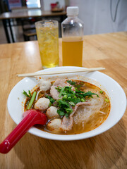 Thai Tom Yum Glass Noodle Soup with Pork Fishballs and Fresh Herbs in White Bowl