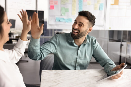 Joyful excited young businessman give high five to female colleague