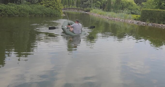 A man sails a rubber boat across an artificial pond. A man fishes in a small rubber boat in a private ornamental pond. A beautiful summer landscape on the water.