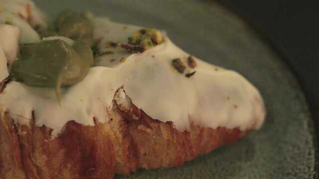 Video en alta resoluci&oacute;n de un croissant relleno de crema de pistacho, cubierto con glaseado blanco y trozos de pistacho. La c&aacute;mara se mueve lentamente mostrando diferentes perspectivas del postre.