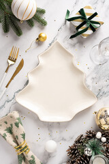 A vertical stylish holiday table featuring a leaf shaped ceramic plate, gold utensils, wrapped...