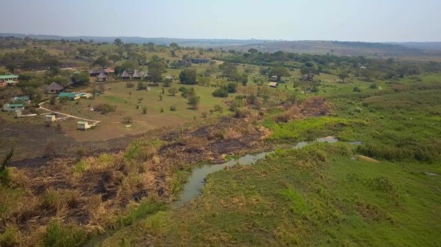 Drone footage captures a safari lodge complex on the riverbank of the Nile in Uganda, surrounded by open grassland, acacia trees and scattered bush.