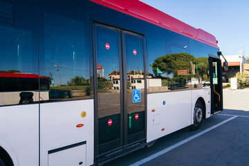 Modern city bus parking on a street, showing reflections on large windows and a disabled access...