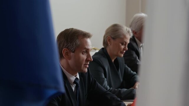 Group of male and female government officials seated during international summit, listening and discussing global political issues at formal meeting
