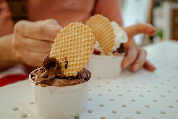 The photo of woman enjoys creamy Italian gelato on a sunny day in Italy. She stands outdoors near a street caf&eacute;, holding ice cream with waffle decor. Summer atmosphere, daylight, travel, Italian city