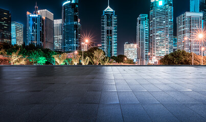 Empty square floor with a modern city skyline and illuminated commercial buildings at night.