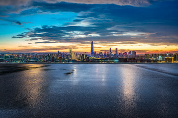 Wet asphalt road and modern buildings skyline at sunset.