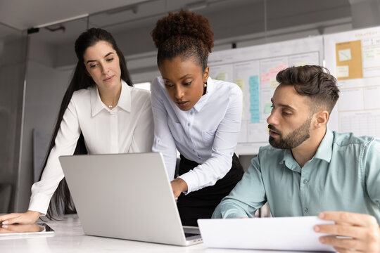 Fototapeta Focused millennial businesswoman teach diverse staff planning on notebook screen