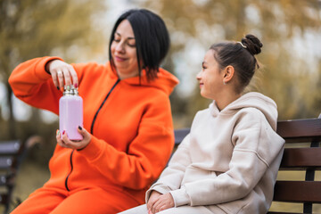 Cute child girl with her mom with thermos cup filled with hot tea on a cold autumn day.