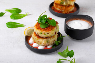 Patties with pollack fish, potato, green pea and cheese filling served with lemon and sour cream sauce on the plate topped with arugula
