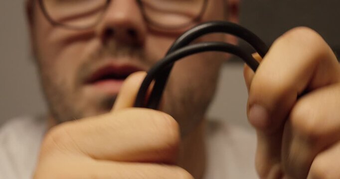 A man bends an elastic black cable close up, demonstrating flexibility and the potential risk of internal cable break or damage.