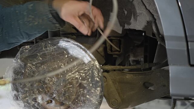 Mechanic uses cavity probe to spray lanolin rust prevention product inside hollow box sections behind protected brake disc