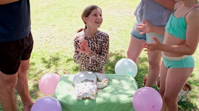 Family sings happy birthday to smiling young girl near cat-shaped cake, slomo
