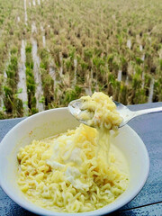 A Bowl of Creamy Instant Noodles and Egg Eaten Outdoors Overlooking a Paddy Field