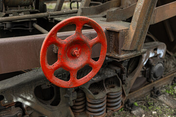 Close-up of a worn red manual brake wheel mounted on a rusted freight wagon, above detailed suspension springs and mechanical components