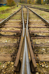 Fototapeta premium Detailed ground-level view of a railway track junction showing the switch point where tracks diverge, surrounded by gravel and wooden ties