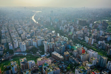 Aerial view of a dense cityscape where buildings cluster tightly, bisected by a winding river reflecting the sky's soft glow, Dhaka, Dhaka Division, Bangladesh.