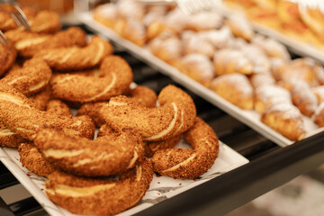 A variety of freshly baked cookies and pastries are arranged on trays in a bakery. Customers enjoy the morning atmosphere while selecting their favorite treats