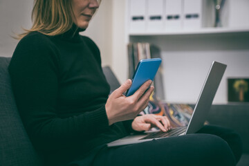 Woman works from home. Girl uses laptop & phone on sofa, comfortable & cozy workspace, flexible work