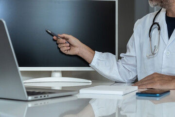 Experienced doctor actively pointing at a blank monitor screen, preparing for a digital presentation or consultation