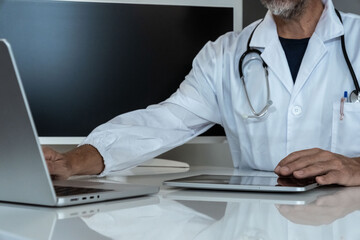 Dedicated doctor in a clinic setting, working with a tablet and laptop, symbolizing modern medical practice
