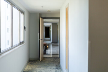 A spacious hotel corridor shows an open door revealing a cozy waiting area. Natural light fills the hallway, enhancing its modern and inviting atmosphere
