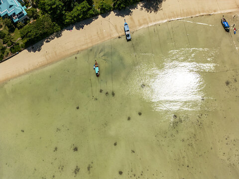 Aerial view of turquoise waters meet the sandy shore, boats rest peacefully under the sun's glare, creating a striking contrast of colors and textures, phi phi, Krabi, Thailand.