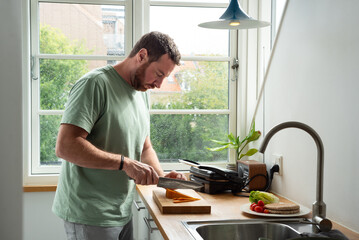 Man slicing cheese for lunch in a Danish style kitchen.