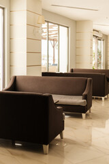 Cozy lounge area features several brown sofas arranged in an inviting manner. Natural light floods in through large windows, creating a warm atmosphere perfect for relaxation