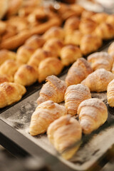 A variety of golden croissants and pastries are neatly arranged on a display in a warm bakery. The fresh aroma of baked goods fills the air, inviting customers to indulge
