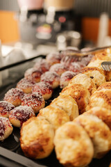 A variety of delicious pastries, including glazed donuts and flaky rolls, are arranged neatly on a bakery tray. The aroma fills the air as customers enjoy their breakfast