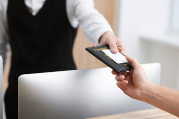 Receptionist giving passport and hotel key card to guest at reception desk indoors, closeup