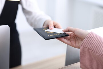 Receptionist giving passport and hotel key card to guest at reception desk indoors, closeup