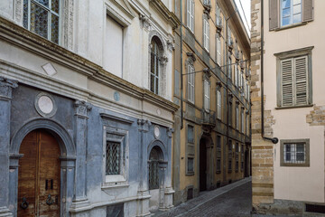 A narrow, dark cobbled alley in Bergamo, Italy, Città Alta, is lined with historic European...