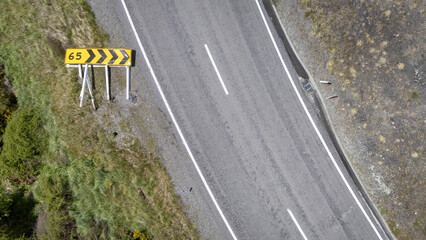 Aerial view of a winding road cutting through the landscape, marked by a yellow and black speed advisory sign felled by storm winds, Hanmer Springs, Canterbury Region, New Zealand.
